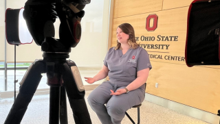 a veterinarian in grey scrubs from OSU sitting in front of cameras