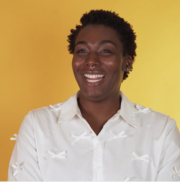 Woman smiling in white shirt with a yellow background.